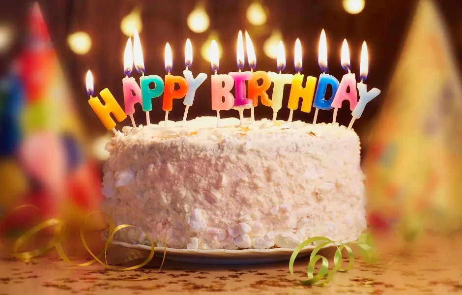 Colorful birthday candles on a frosted cake with party decor and warm lights, ideal for celebrations.
