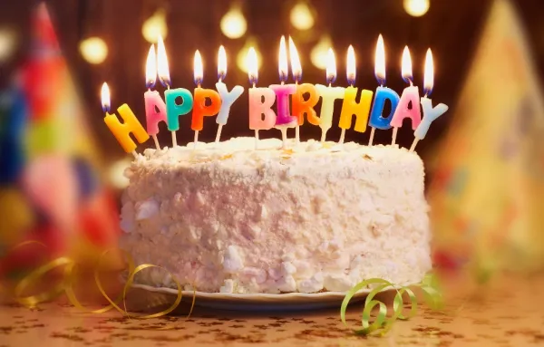 Colorful birthday candles on a frosted cake with party decor and warm lights, ideal for celebrations.