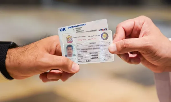 Hands exchanging a UK driving license and a UAE driving license