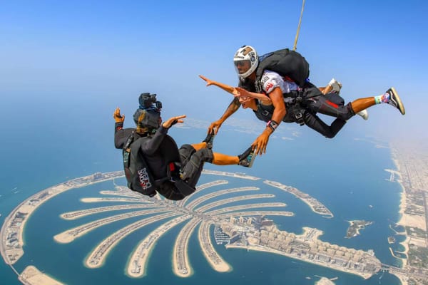 Two skydivers holding hands above Palm Jumeirah in Dubai with blue sky and ocean in the background